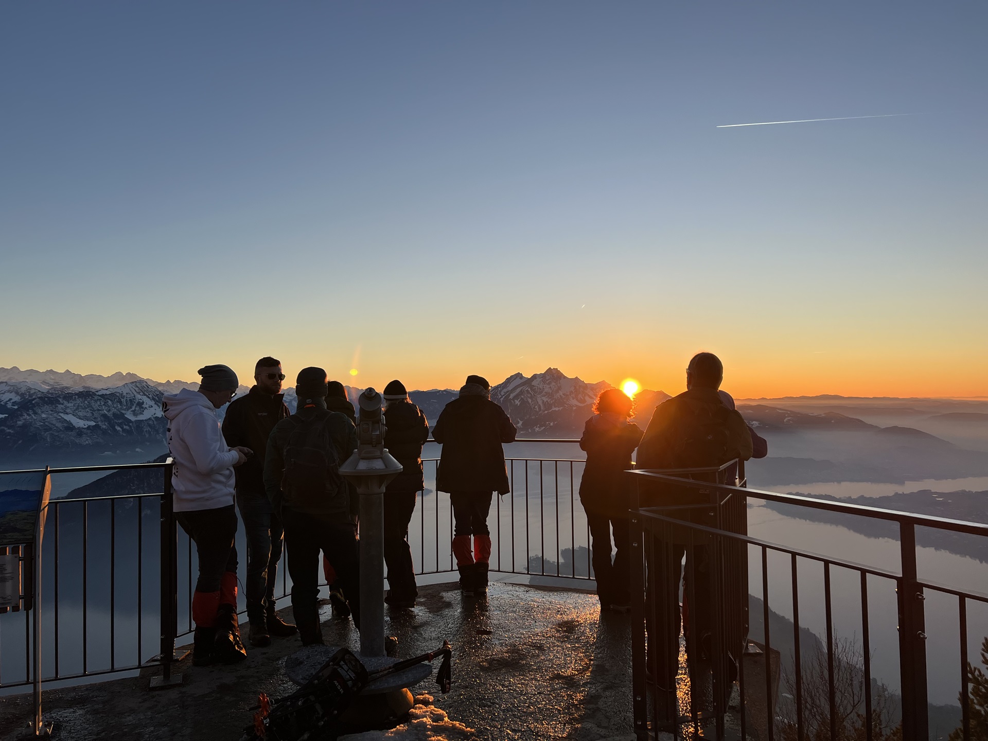 Eine Gruppe von Leuten stehen bei Sonnenuntergang beim Aussichtspunkt "Känzeli", vor ihnen der Pilatus mit der untergehenden Sonne