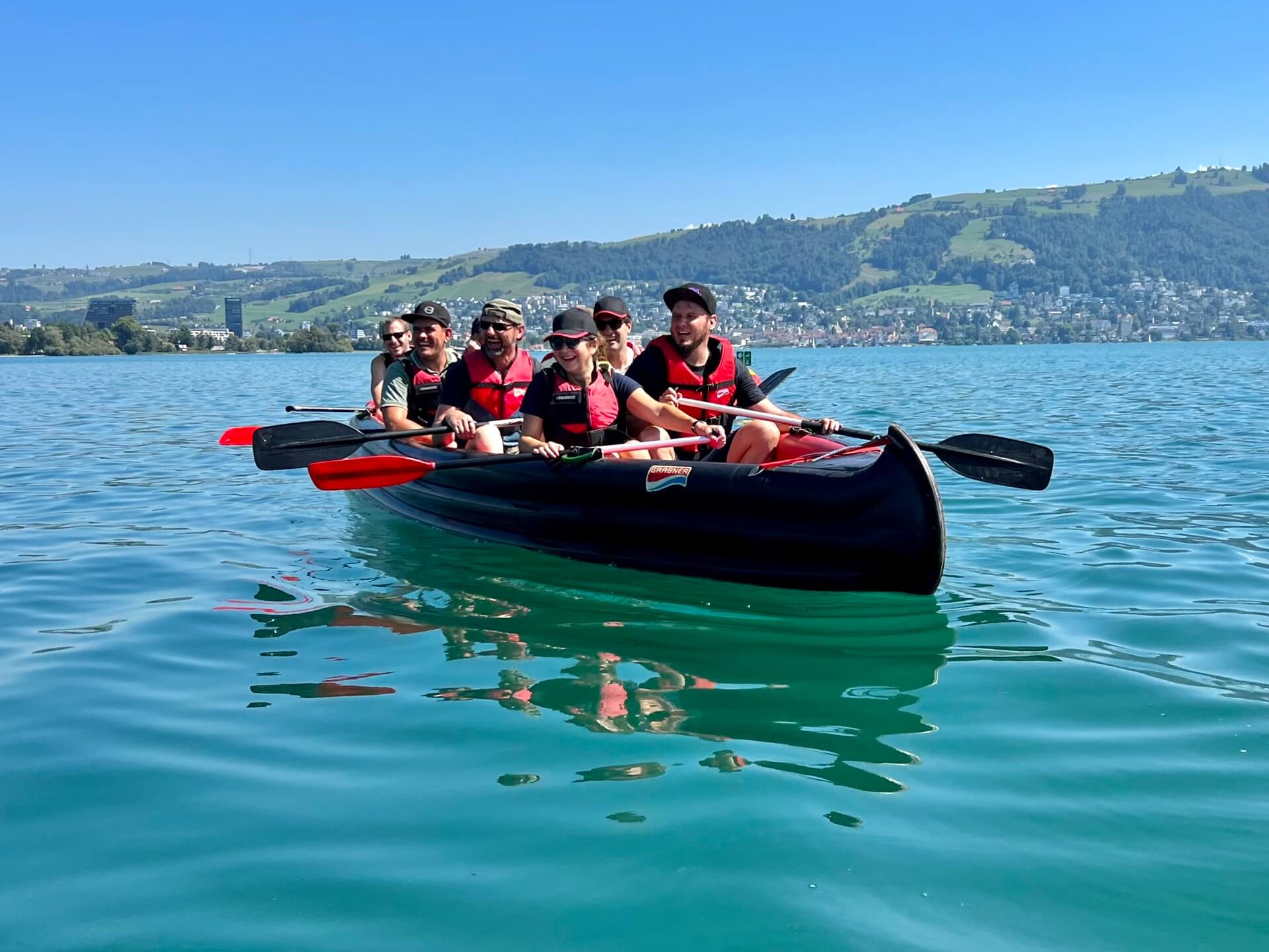 Ein Grosskanadier-Kanu auf dem See, 6 Leute sitzen im Kanu, im Hintergrund ist in der Weite das Ufer ersichtlich