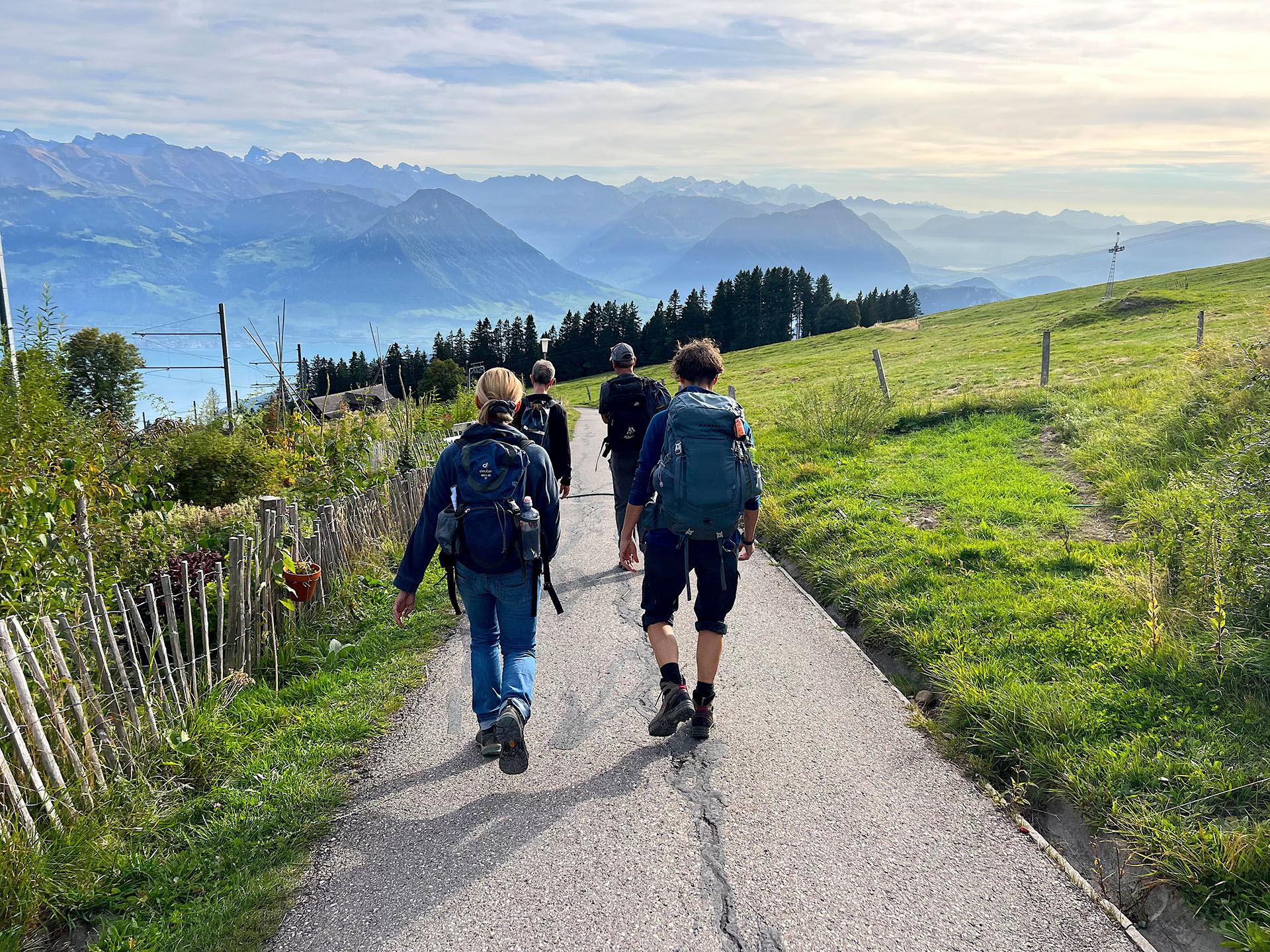 Vier Leuten befinden sich auf Rigi Staffelhöhe und laufen auf dem asphaltierten Weg entlang des Kräutergartens, vor ihnen die Aussicht auf das Buochser- und Stanserhorn.