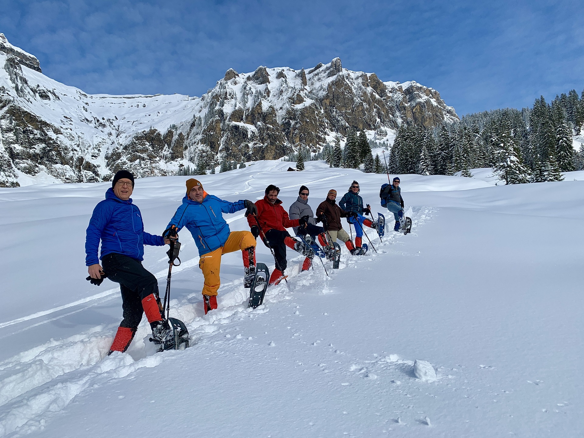 7 Leute stehen mit Schneeschuhen im Schnee und lachen in die Kamera